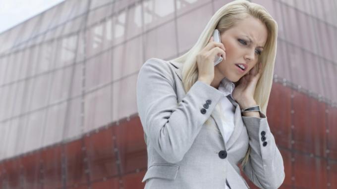 Mujer con TDAH escuchando a alguien por teléfono celular y enojándose frente a un edificio alto