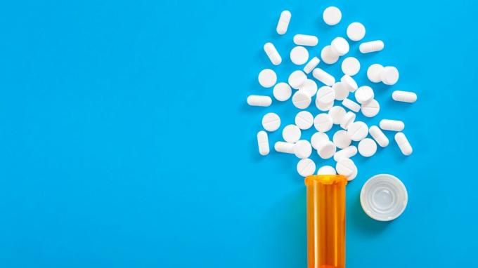 Concepto de medicamentos, analgésicos opioides y medicamentos recetados con vista superior del frasco de receta naranja de píldoras de oxicodona e hidrocodona derramadas sobre un fondo azul con espacio de copia